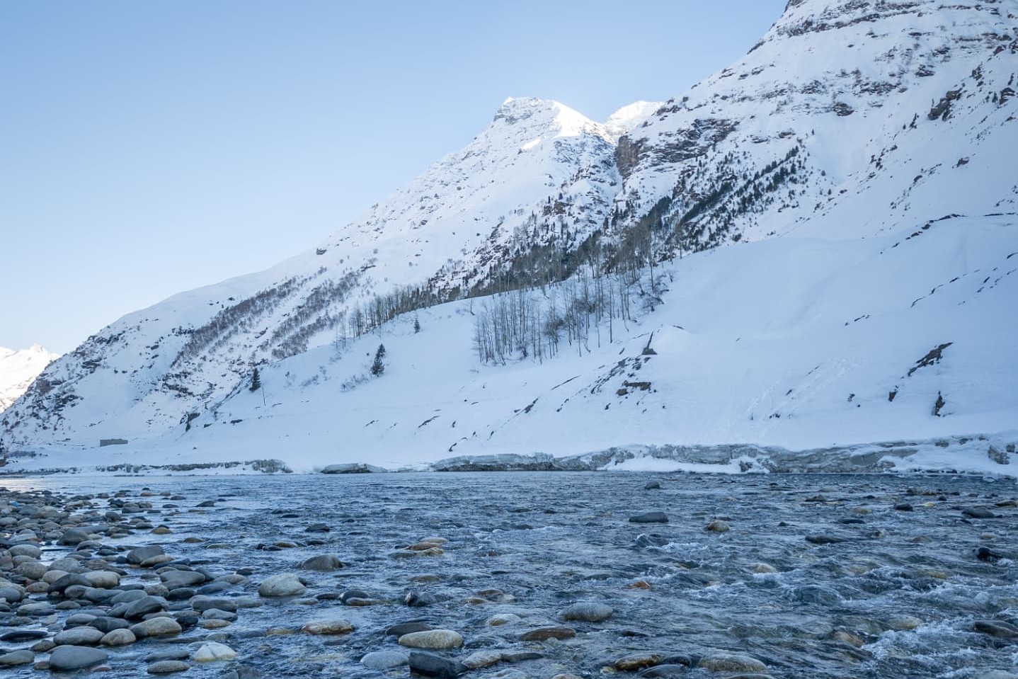 Clear mountain river flowing past snow-covered slopes