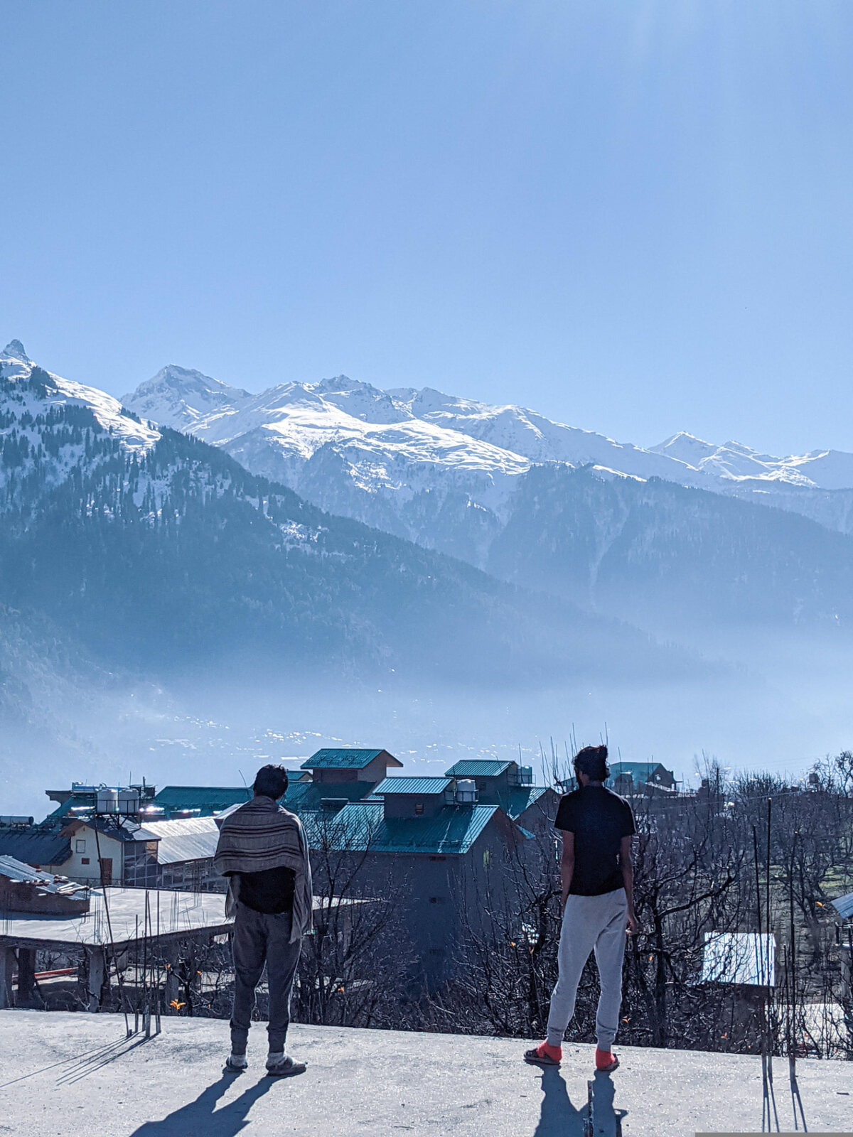 Two travellers taking in a view of snowy peaks and a misty valley