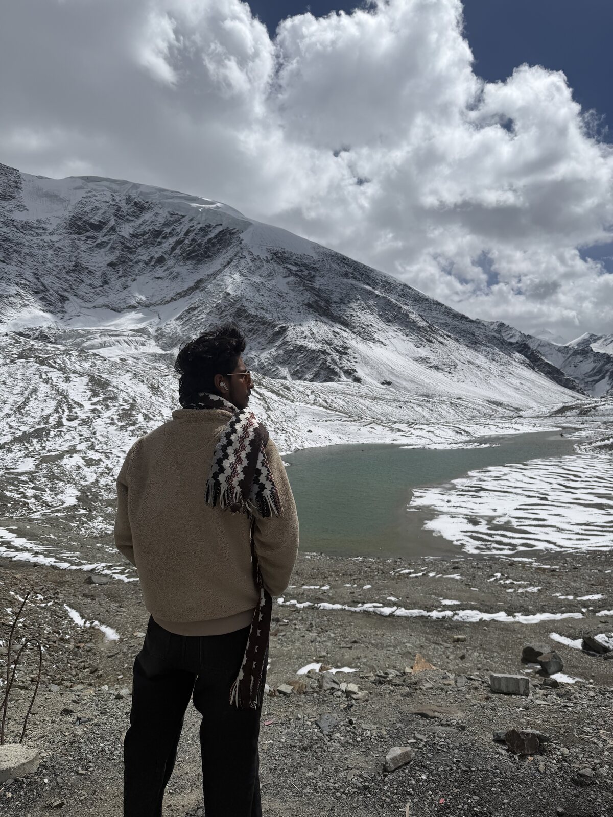 Traveller standing by a half-frozen mountain lake